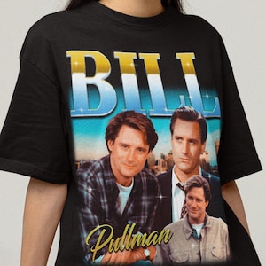 Puede incluir: Camiseta negra con un gráfico retro del actor Bill Pullman. El diseño incluye el nombre "BILL" en oro y azul, imágenes del actor y su firma. La camiseta tiene cuello redondo.