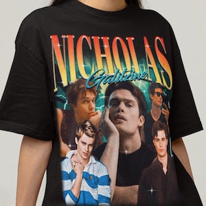 May include: Black t-shirt featuring a collage of images of a man with the text "Nicholas Galitzine" in a retro style font. The shirt has a crew neck and short sleeves.
