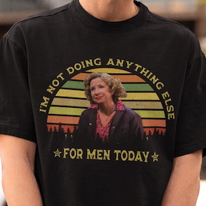Puede incluir: Camiseta negra con un diseño gráfico circular que presenta la imagen de una mujer, un diseño de puesta de sol y el texto "I'M NOT DOING ANYTHING ELSE FOR MEN TODAY". La camiseta es de manga corta y cuello redondo.