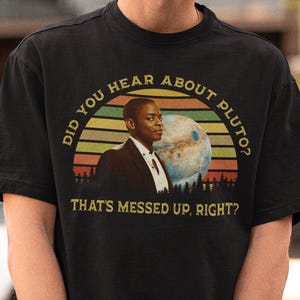 May include: Black t-shirt with a graphic featuring a man, a planet, and the text "DID YOU HEAR ABOUT PLUTO? THAT'S MESSED UP, RIGHT?" The design is set against a sunset-style background.