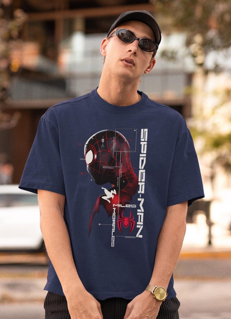 May include: Navy blue t-shirt featuring a graphic of Spider-Man's head and torso in red and black, with the text "SPIDER-MAN" and "MILES MORALES" in white. The Spider-Man logo is also visible.