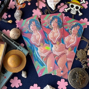 Può includere: Tre segnalibri colorati raffiguranti una donna in abito rosso e bianco, con i capelli blu. L'immagine include anche un cappello di paglia, un orologio da tasca e un ciondolo a forma di teschio, il tutto su una superficie blu con ritagli di fiori rosa.