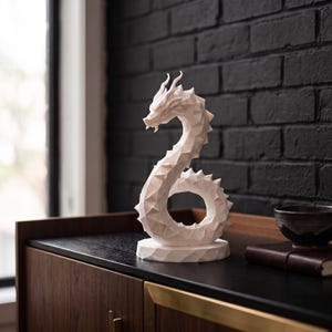 May include: A white, low-poly geometric dragon sculpture standing on a circular base. The dragon features a curved, serpentine body with sharp, angular facets and spikes along its back, captured in a solid, matte white finish with a distinct head.