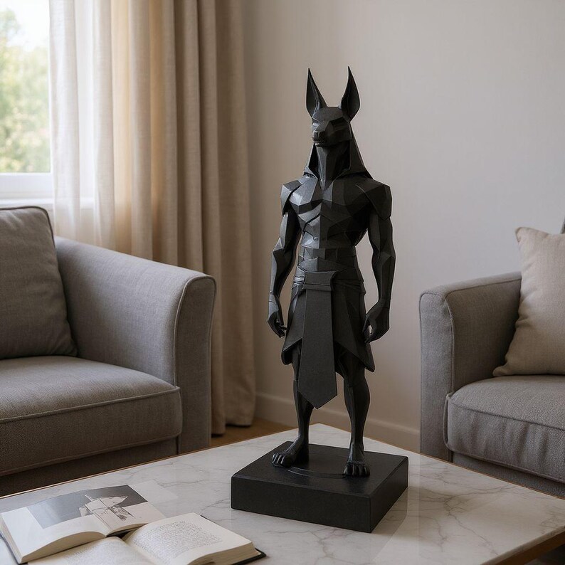 May include: A matte black, geometric-style sculpture of the Egyptian deity Anubis, depicted with a jackal head and human-like muscular torso. The figure stands on a rectangular black base, wearing a traditional kilt-like garment.