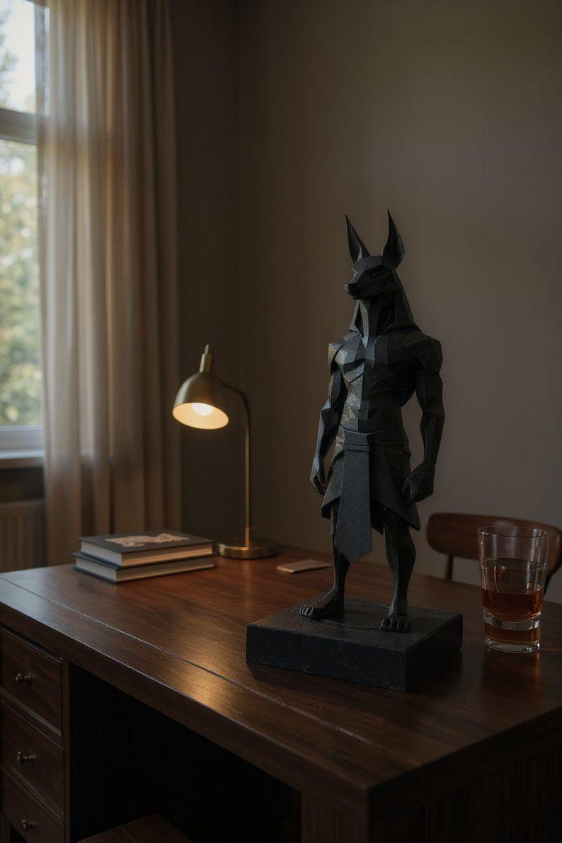 May include: A matte black, geometric, low-poly style sculpture of the Egyptian deity Anubis, depicted with a jackal head and human-like muscular torso, standing on a rectangular base. The figure features sharp, angular facets throughout its form.