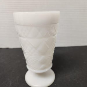 May include: A white, vintage-style glass with a diamond pattern. The glass has a round base and a flared top. The glass is made of opaque white glass and is likely used for serving beverages.