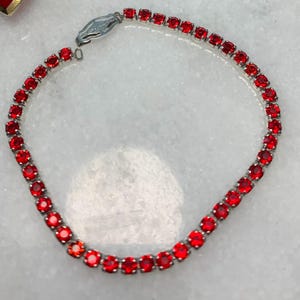 May include: A silver-toned bracelet featuring a series of vibrant red gemstones. The gemstones are round and set closely together, creating a continuous line of color. The clasp is a simple, secure design.