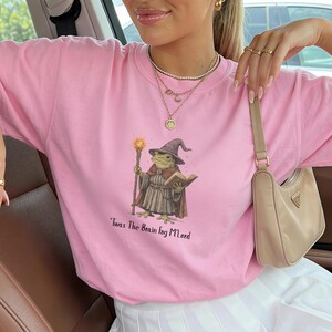 K&ouml;nnte beinhalten: Hellrosa T-Shirt mit einer Illustration eines Froschzauberers, der einen Stab und ein Buch h&auml;lt. Der Frosch tr&auml;gt einen Zaubererhut und einen Umhang. Der Text "'Twas The Brain Fog M'Lord" ist darunter gedruckt.
