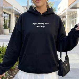 Peut inclure: Un sweat-shirt &agrave; capuche noir avec le texte blanc "my anxiety has anxiety" imprim&eacute; sur la poitrine. Le v&ecirc;tement comprend une poche kangourou &agrave; l'avant, des manches longues avec des poignets c&ocirc;tel&eacute;s et une capuche &agrave; cordon de serrage.