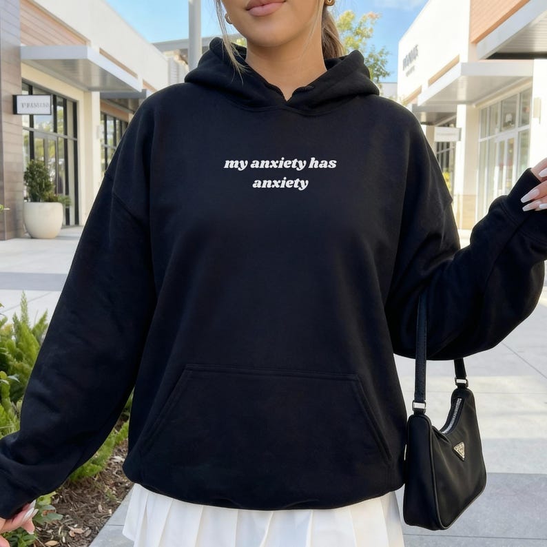 Peut inclure: Un sweat-shirt &agrave; capuche noir avec le texte blanc "my anxiety has anxiety" imprim&eacute; sur la poitrine. Le v&ecirc;tement comprend une poche kangourou &agrave; l'avant, des manches longues avec des poignets c&ocirc;tel&eacute;s et une capuche &agrave; cordon de serrage.