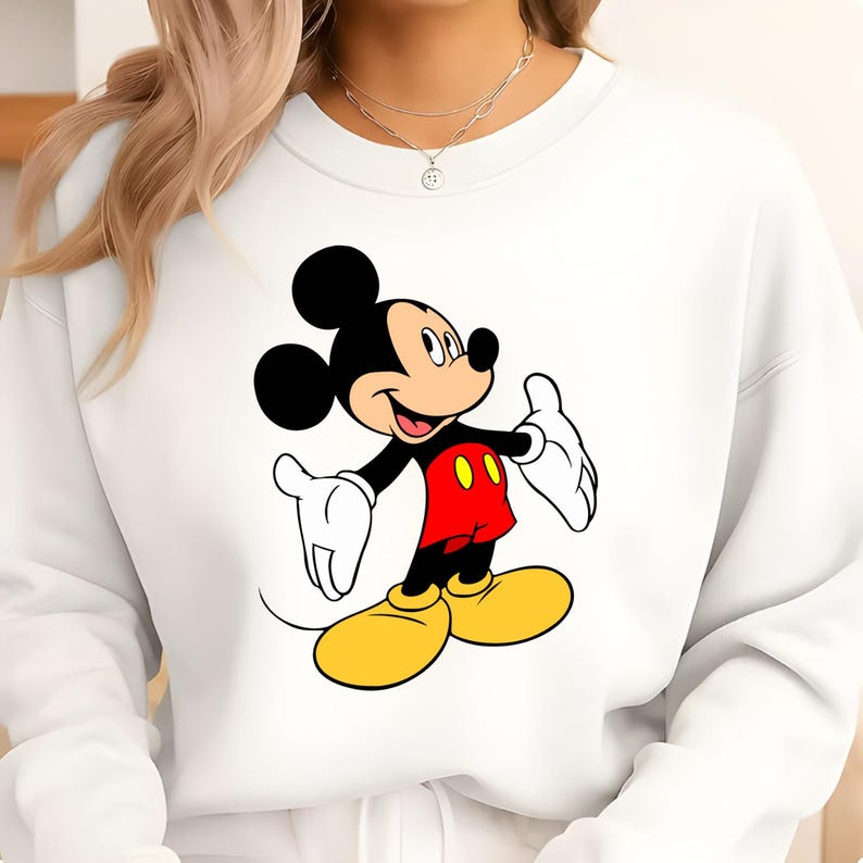 K&ouml;nnte beinhalten: Wei&szlig;es Sweatshirt mit einer Mickey Mouse-Grafik. Die Zeichentrickmaus wird mit schwarzen Ohren, einem schwarzen K&ouml;rper, roten Shorts, gelben Schuhen und wei&szlig;en Handschuhen gezeigt. Das Sweatshirt ist ein l&auml;ssiger Stil.