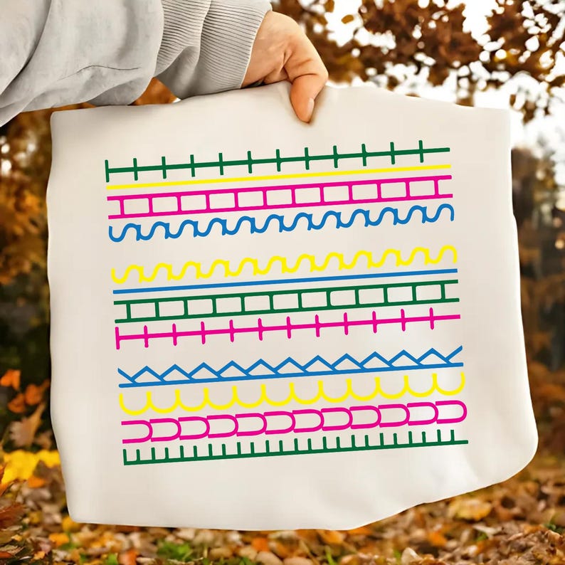 May include: A white tote bag with a colourful, geometric pattern. The design includes horizontal lines in green, yellow, pink, and blue, creating a vibrant aesthetic. The bag is held by a person.