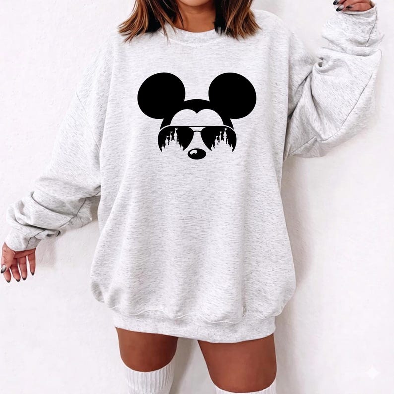 Puede incluir: Sudadera gris claro con un gr&aacute;fico negro de Mickey Mouse con gafas de sol. El gr&aacute;fico es una silueta de la cara de Mickey con sus ic&oacute;nicas orejas. La sudadera tiene cuello redondo y mangas largas.