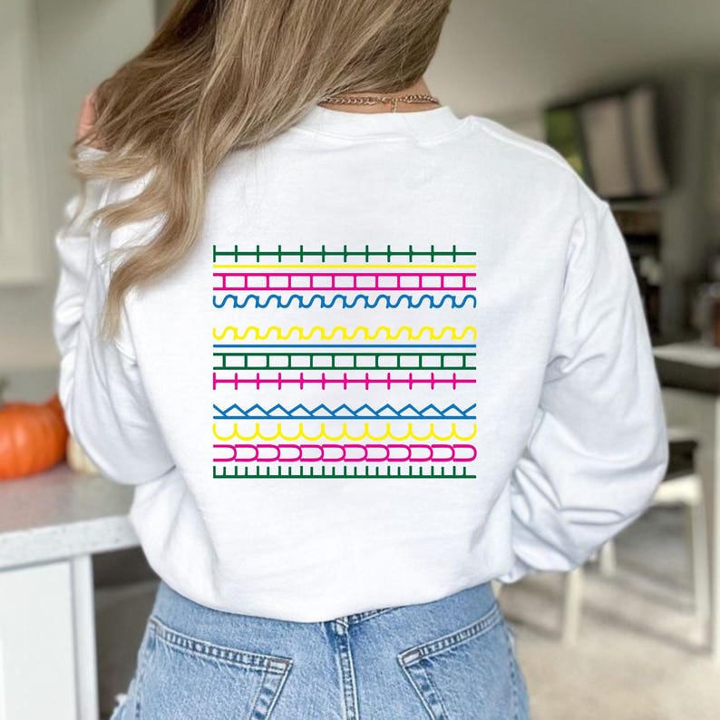 May include: White sweatshirt with a colourful geometric design on the back. The design features horizontal rows of various shapes and colours, including green, pink, yellow, and blue. A casual, everyday garment.