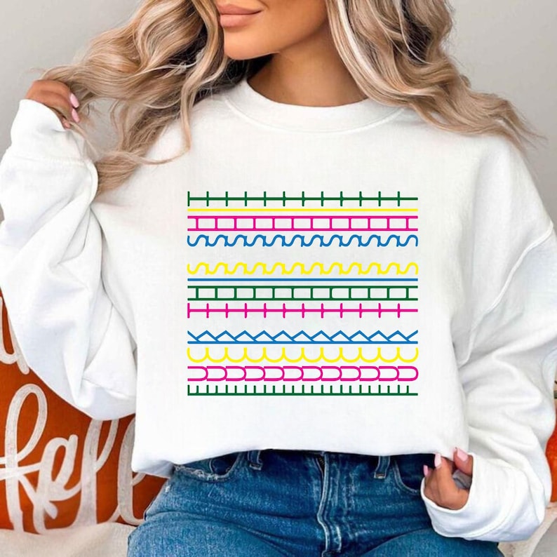 May include: White sweatshirt with a vibrant geometric pattern. The design incorporates horizontal rows of green, pink, yellow, blue, and pink lines in diverse patterns. A casual, comfortable style of clothing.