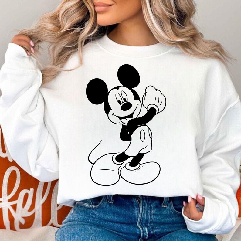 May include: White sweatshirt featuring a black and white graphic of Mickey Mouse in a playful pose. The cartoon character is smiling and wearing white gloves and shoes. The sweatshirt is a casual style.