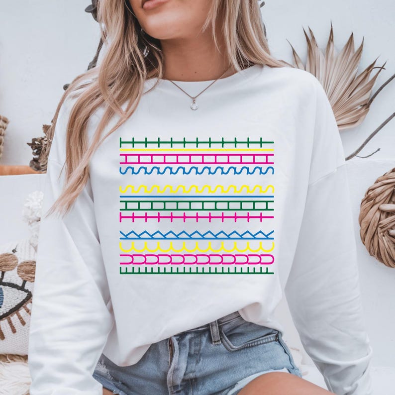 May include: White sweatshirt with a colourful geometric pattern. The design features horizontal lines in green, pink, yellow, and blue, creating a vibrant look. The sweatshirt is a casual, comfortable garment.