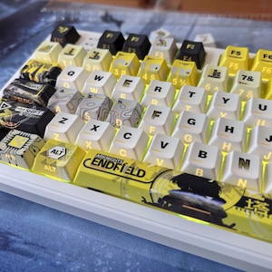 May include: A custom mechanical keyboard with yellow and white keycaps. The keycaps feature various designs, including circuit board patterns, topographic maps, and the text "ARKNIGHTS ENDFIELD". The keyboard has a white frame and is backlit.
