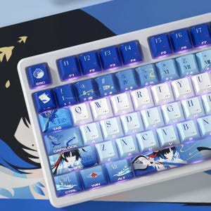 May include: A mechanical keyboard featuring a white frame and a custom keycap set in shades of blue and white. The keycaps display alphanumeric characters, function keys, and decorative anime-style illustrations, including a character on the shift key.