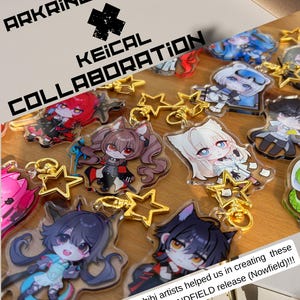 May include: A collection of chibi character keychains with gold star-shaped charms. The keychains feature various anime-style characters in different poses and colors. The text "ARKRINEDESIGNS KEICAL COLLABORATION" is displayed, along with a message about the ENDFIELD release.
