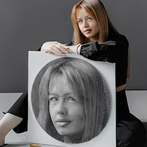 Könnte beinhalten: Eine Person in schwarzer Kleidung hält ein Schwarz-Weiß-Porträt einer Frau in einem kreisförmigen Rahmen. Das Porträt befindet sich auf einer weißen Leinwand vor grauem Hintergrund.