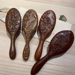 Puede incluir: Cuatro cepillos de madera para el cabello con intrincados diseños tallados. Los cepillos presentan detallados motivos florales, de aves y paisajes. La madera tiene un color marrón cálido y rico, y cada cepillo tiene un mango largo y curvado.