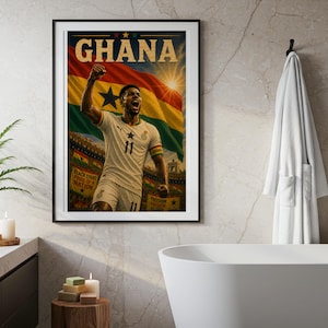 May include: A framed vertical poster featuring a soccer player in a white jersey with the number 11, celebrating in front of a large Ghanaian flag. The word GHANA is printed in bold gold letters at the top, with a stadium crowd visible below.