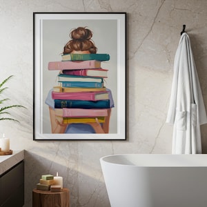 Könnte beinhalten: Ein gerahmter Kunstdruck, der eine Person mit braunem Dutt zeigt, die einen hohen Stapel bunter Bücher hält. Die Bücher in Türkis, Pink, Blau und Gelb verdecken das Gesicht der Person. Das Kunstwerk befindet sich in einem schwarzen Rahmen.