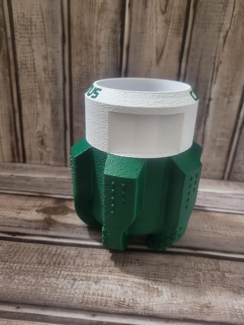 May include: A green and white 3D-printed planter. The planter has a textured green base with a white rim and the text "US" visible. The planter is designed with a unique, geometric shape.