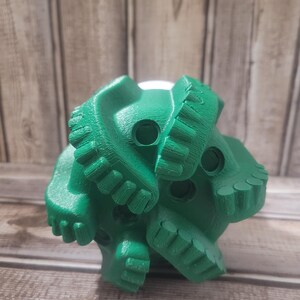 May include: A bright green, multi-faceted object with a complex, textured surface. The object has several circular openings and a series of tooth-like protrusions. The item is likely a component or tool, possibly for industrial or construction purposes.