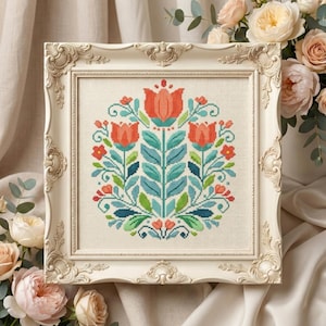 May include: A framed cross-stitch floral design. The artwork features a symmetrical arrangement of stylized flowers in shades of orange, teal, and green, set against a cream-colored background. The frame is ornate, with a cream-colored finish.