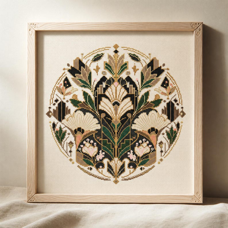 K&ouml;nnte beinhalten: Eine quadratisch gerahmte Kreuzstichstickerei mit einem kreisf&ouml;rmigen botanischen Muster. Das Design zeigt symmetrische Blumen- und Blattmotive in den Farben Dunkelgr&uuml;n, Creme, Schwarz und zartem Rosa auf einem hellbeigen Stoffhintergrund.