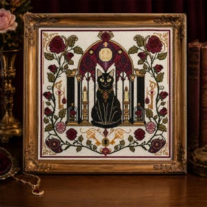 Puede incluir: Un bordado de punto de cruz en un marco dorado ornamentado que muestra un gato negro sentado en un arco gótico. El diseño incluye rosas rojas, hojas verdes, dos velas encendidas, llaves doradas y una luna llena sobre tela color crema.