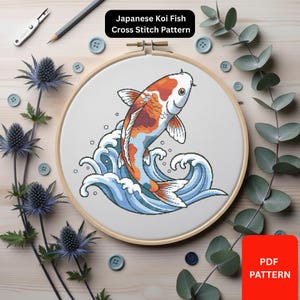 May include: A cross-stitch pattern featuring a Japanese koi fish leaping from blue and white waves. The fish has orange, white, and brown markings. The text "Japanese Koi Fish Cross Stitch Pattern" is displayed above the design. The pattern is in a wooden embroidery hoop.