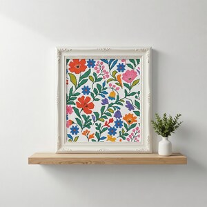 May include: A framed floral cross-stitch pattern featuring a vibrant array of flowers in red, pink, orange, blue, and purple, set against a white background. The artwork is displayed in a white ornate frame, resting on a wooden shelf.