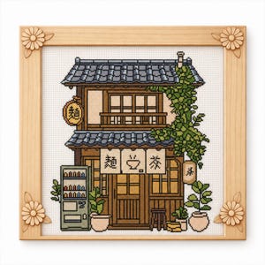 May include: Cross-stitch of a Japanese tea house in a wooden frame. The building is brown with a grey tiled roof, green vines, and Japanese characters. A vending machine and potted plants are in front.
