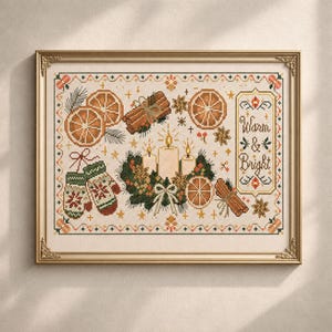 May include: A framed cross-stitch embroidery featuring the text "Warm & Bright" surrounded by motifs of orange slices, cinnamon sticks, star anise, a candle wreath, and a pair of patterned mittens in shades of green, red, orange, and brown.