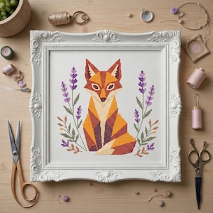 May include: A framed cross-stitch of a geometric fox in shades of orange, brown, and white, surrounded by purple lavender. The artwork is in a white ornate frame, set against a light wood surface.