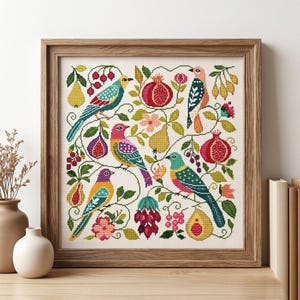 May include: A framed cross-stitch artwork featuring colorful birds, pomegranates, pears, and flowers. The birds have vibrant blue, yellow, pink, and green plumage. The artwork is set against a cream-colored background and framed in a light brown wooden frame.