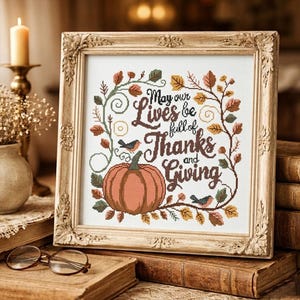 Könnte beinhalten: Ein gerahmtes Kreuzstichbild mit einem Kürbis und dem Text "May our Lives be full of Thanks and Giving". Das Kunstwerk ist von Herbstblättern und zwei kleinen Vögeln umgeben, in einem dekorativen Goldrahmen.