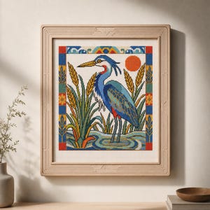 May include: A framed cross-stitch embroidery featuring a blue and grey heron standing in water among tall yellow reeds. The scene includes a bright orange sun and a decorative border with geometric patterns in red, blue, yellow, and green colors.