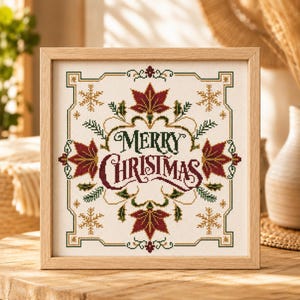 Puede incluir: Un bordado en punto de cruz en un marco cuadrado con el texto Merry Christmas en letras de color rojo oscuro y verde. El diseño está rodeado de hojas de arce rojo oscuro, ramas de pino verdes y copos de nieve dorados sobre tela crema.