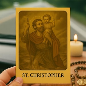 May include: A yellow card featuring an illustration of St. Christopher carrying a child, with a halo above each figure. The card has the text "ST. CHRISTOPHER" at the bottom. A lit candle and rosary beads are in the background.