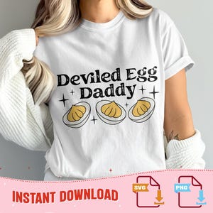 May include: White t-shirt with the text "Deviled Egg Daddy" in black, accompanied by three illustrations of deviled eggs. The design includes star accents. The phrase "Instant Download" is at the bottom, along with SVG and PNG icons.