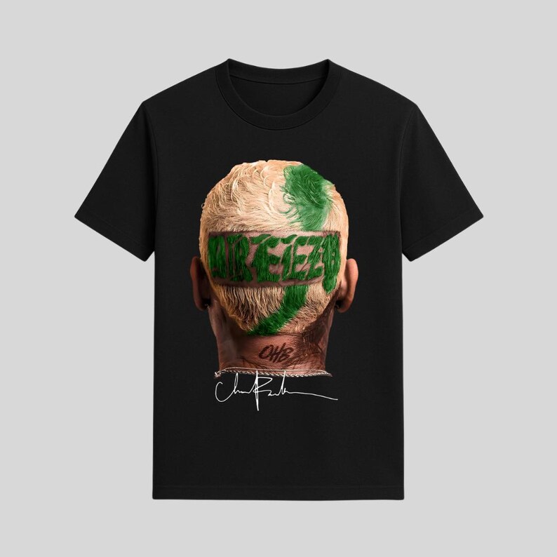 May include: Black t-shirt featuring a graphic of a person's head with blonde hair and green accents. The word "REEZY" is printed across the back of the head in green. A signature is visible below the head.
