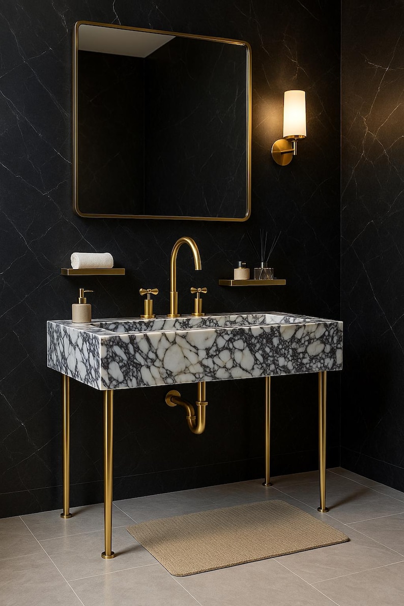Op de afbeelding: Een moderne badkamerwastafel met een marmeren aanrechtblad en gouden armaturen. De wastafel wordt ondersteund door gouden poten en heeft een bijpassende gouden kraan en spiegel. Er ligt een klein tapijt op de vloer.