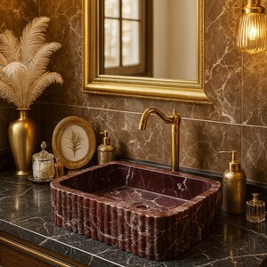 Puede incluir: Un lujoso mueble de ba&ntilde;o con un lavabo rectangular de m&aacute;rmol burdeos. El lavabo est&aacute; sobre una encimera oscura con accesorios dorados, incluyendo un grifo y l&aacute;mparas colgantes. Un espejo con marco dorado y objetos decorativos completan el elegante dise&ntilde;o.