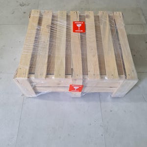Puede incluir: Un palet de env&iacute;o de madera envuelto en pl&aacute;stico transparente. El palet tiene varias lamas y soportes de madera. Se ven dos pegatinas rojas de "Fr&aacute;gil".