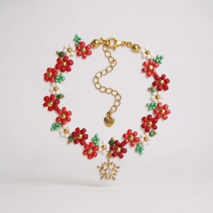 Puede incluir: Una pulsera de cuentas con detalles florales rojos, blancos y verdes. La cadena dorada incluye un dije en forma de corazón y un colgante de copo de nieve. La pulsera, con temática floral, es ideal para añadir un toque de elegancia.