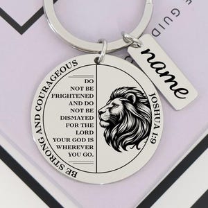 May include: A silver-colored keychain with a round pendant featuring a lion's head and the text "BE STRONG AND COURAGEOUS." A smaller tag reads "name." The text "JOSHUA 1:9" is also visible.